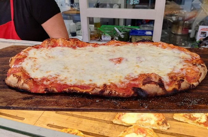 A long tray of Roman pizza, cut and served on a wooden board